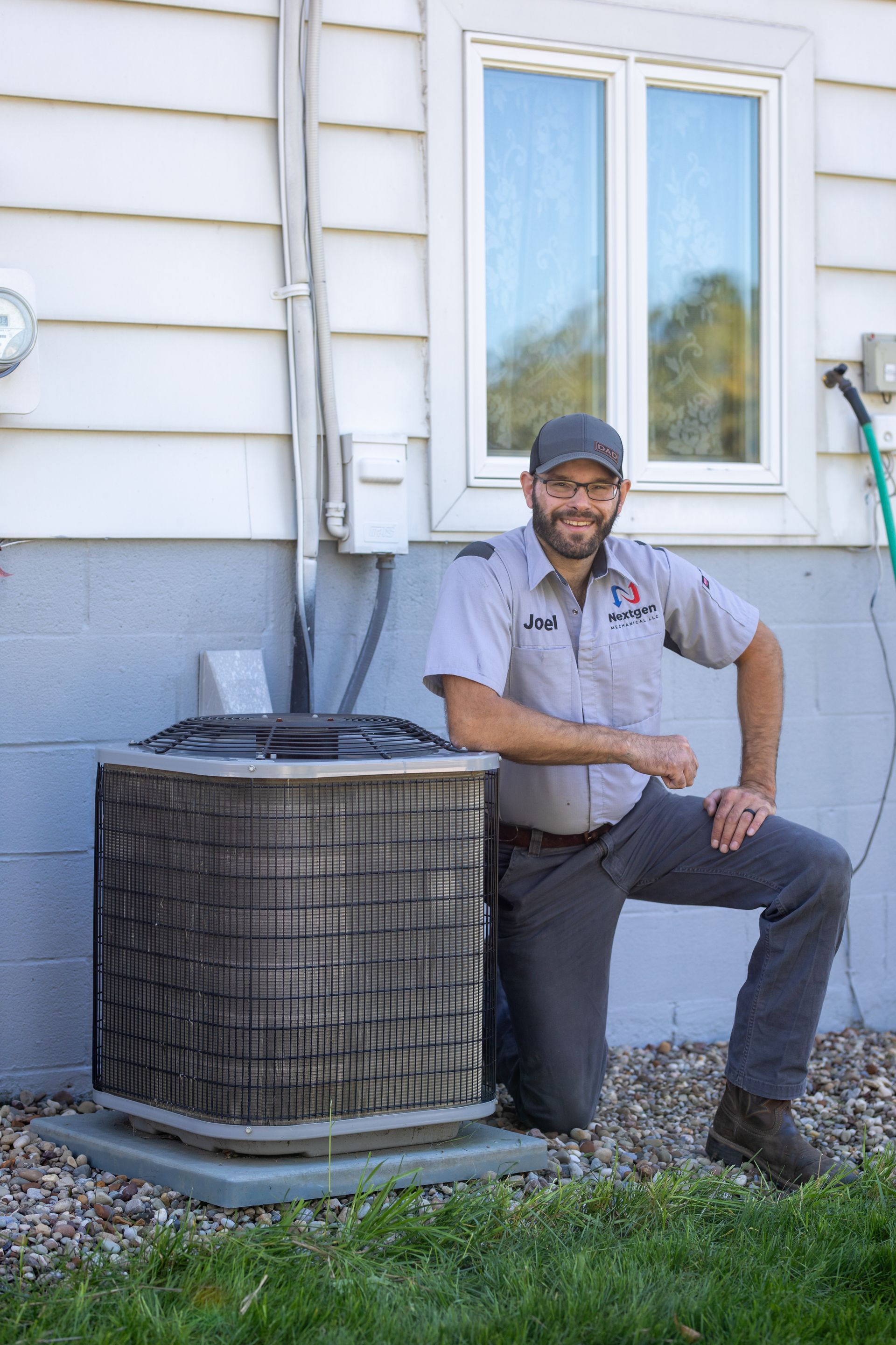 HVAC technician using tools on an outdoor AC unit. Outdoors with concrete wall and gravel.