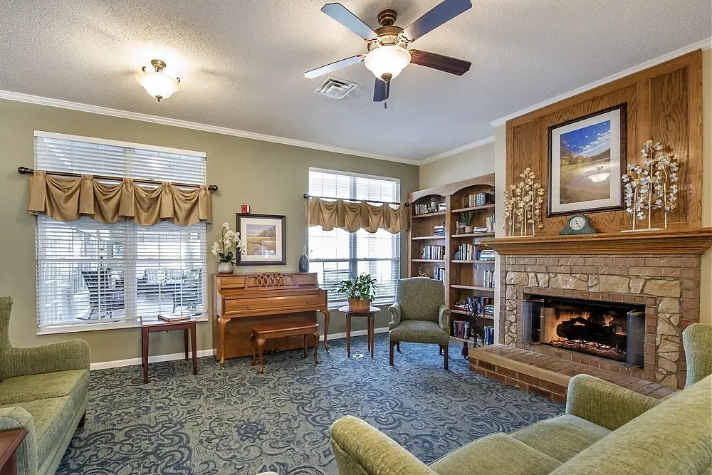 Cozy living room with fireplace, piano, green chairs, and blue patterned carpet