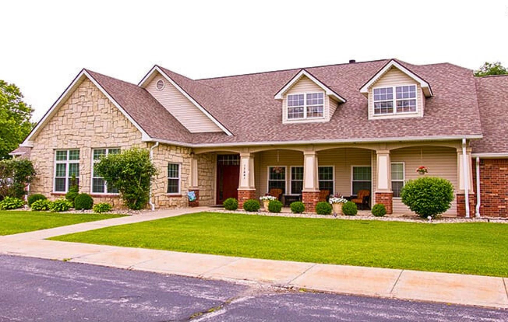 Large brick suburban house with a gabled roof, front porch, manicured lawn, and driveway