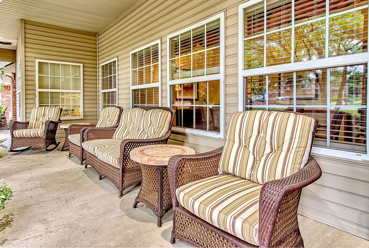 Covered porch with wicker seating and striped cushions beside large windows