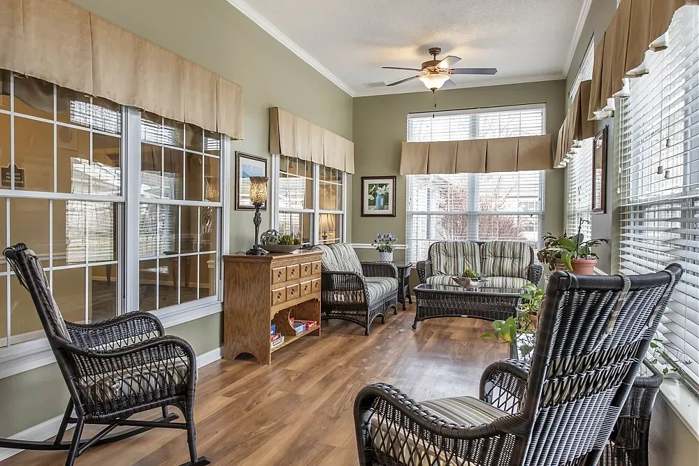 Sunroom with wicker chairs, large windows, wood floor, and a ceiling fan letting in bright daylight