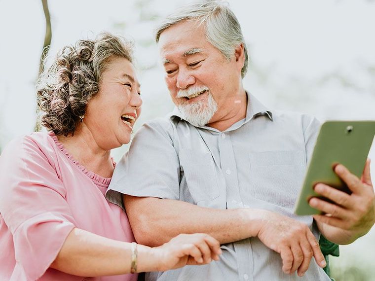 Two people smiling and looking at a tablet together, one holding it in a bright indoor setting