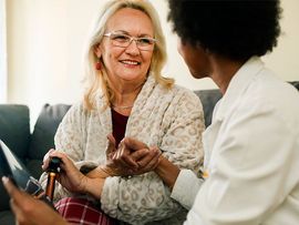 Two women smiling and holding hands on a couch in a bright living room
