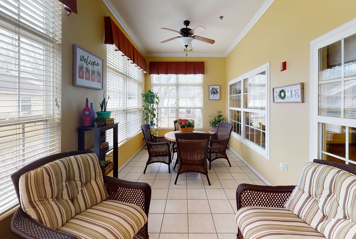 Sunlit enclosed porch with striped armchairs, wicker table and chairs, tiled floor, and large windows