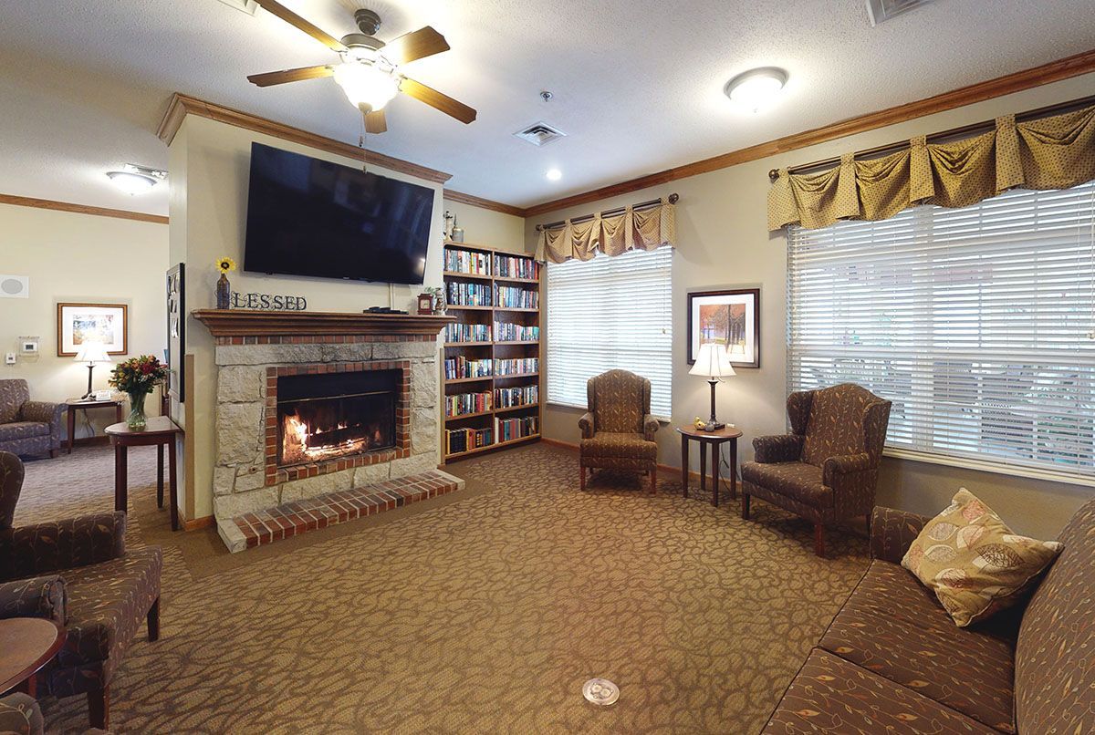 Cozy living room with a lit fireplace, ceiling fan, armchairs, large TV, and bay window seating