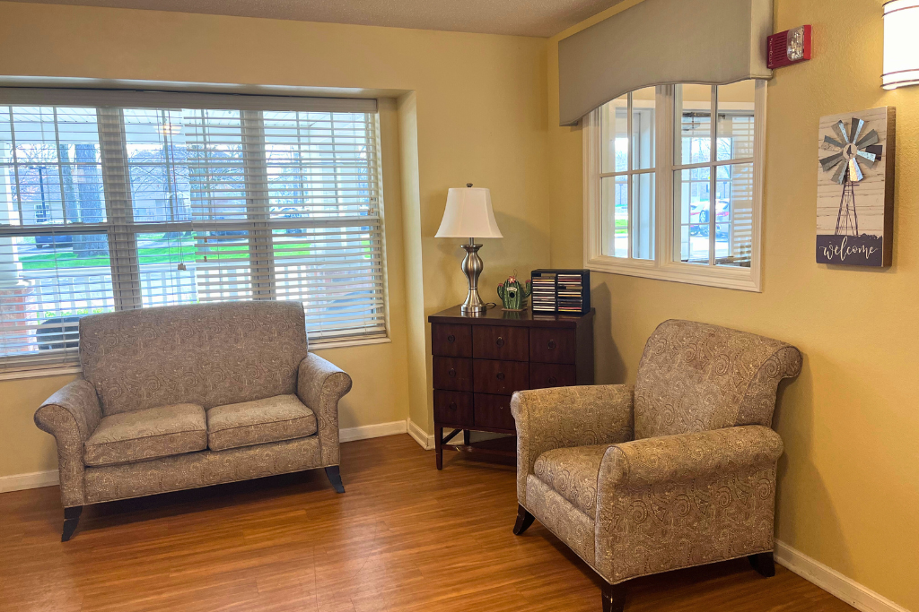 Cozy living room with two patterned armchairs, sofa, lamp, window, and hardwood floor