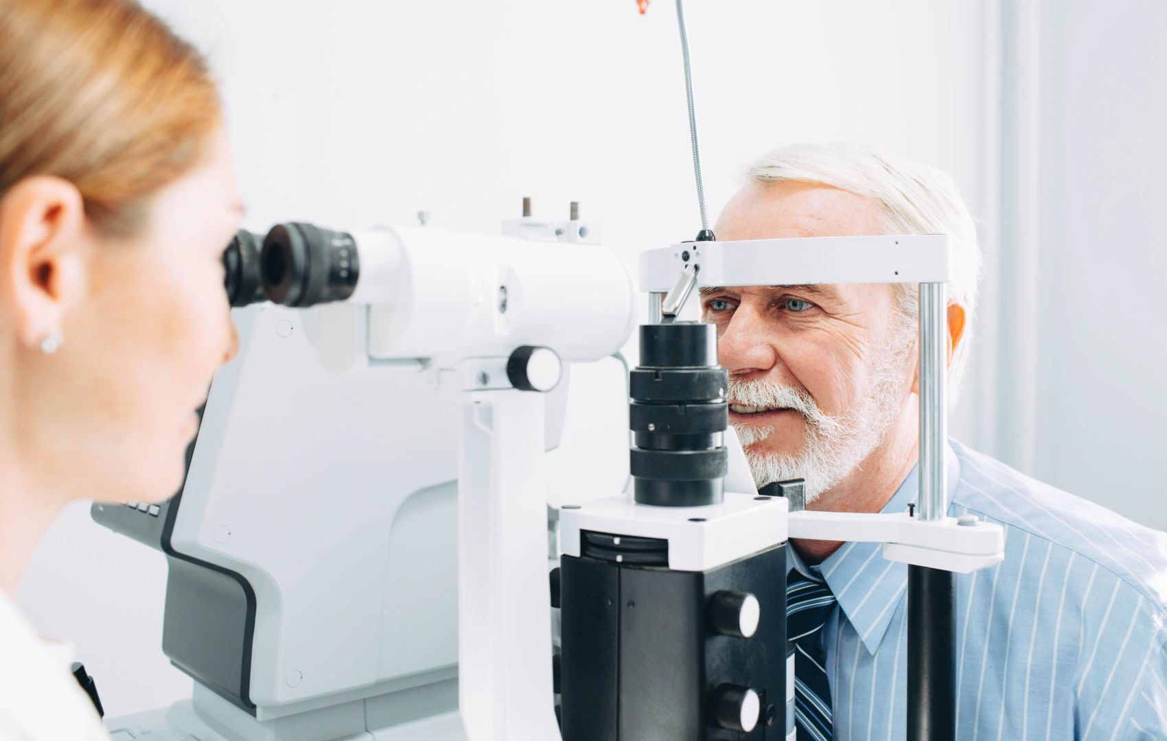 Eye doctor examining an older patient with a slit-lamp machine in a bright clinic