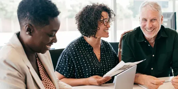 Three coworkers smiling and reviewing documents at a bright office table