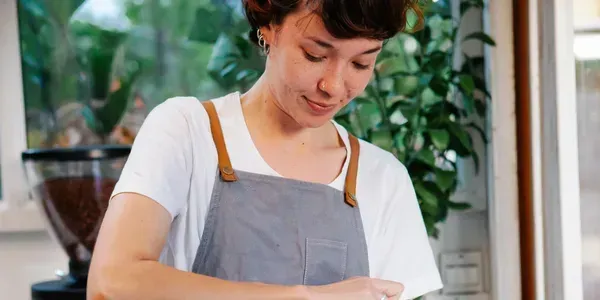 Person in a gray apron working in a bright kitchen with plants in the background