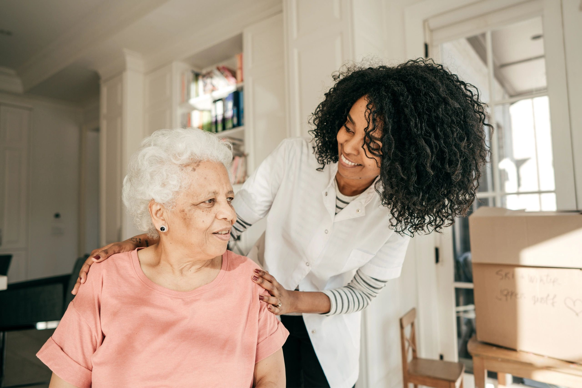 Woman smiling while helping an elderly person in a bright kitchen during a move