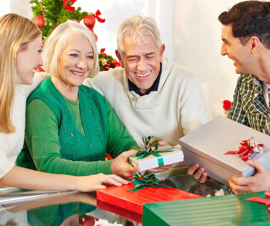 People exchanging wrapped gifts at a holiday table, smiling and chatting in a festive room