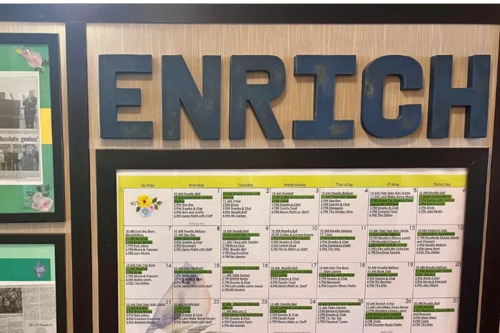 Classroom bulletin board with large blue “ENRICH” letters above a calendar-style schedule chart.