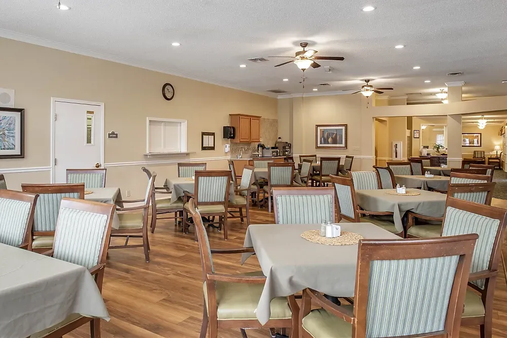 Bright dining room with tables, chairs, booths, and ceiling fans in a senior living cafeteria