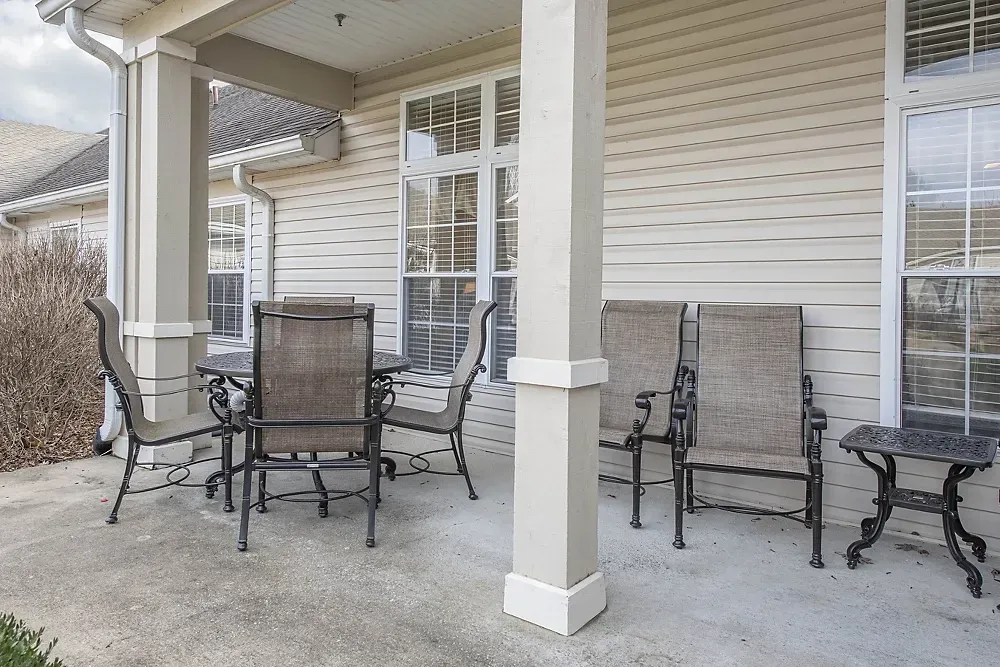 Covered patio with outdoor dining table and chairs beside a beige house with white columns