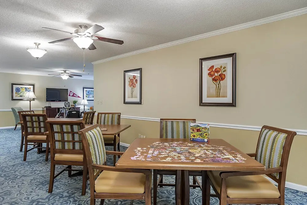 Dining room with wooden tables and chairs, beige walls, framed art, and ceiling fans.