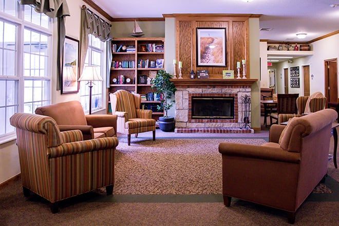 Cozy living room with armchairs, a brick fireplace, built-in bookshelf, and large windows