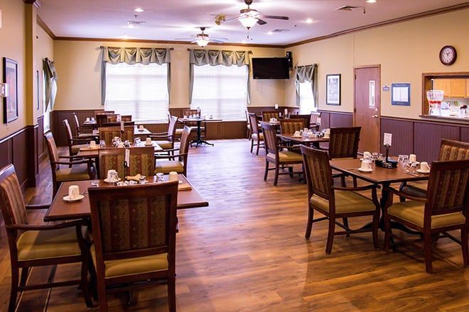 Empty dining room with wooden tables and chairs, wood floors, and large windows with curtains