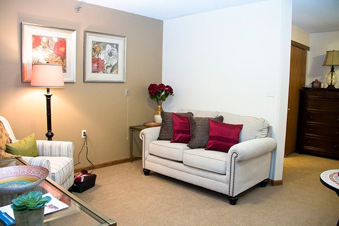 Bright living room with beige sofa, red pillows, lamp, framed art, and flowers on a side table