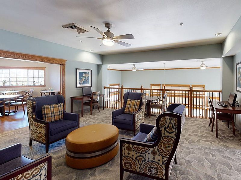 Spacious lounge with patterned chairs, round ottoman, ceiling fans, and balcony railing overlooking a lower level