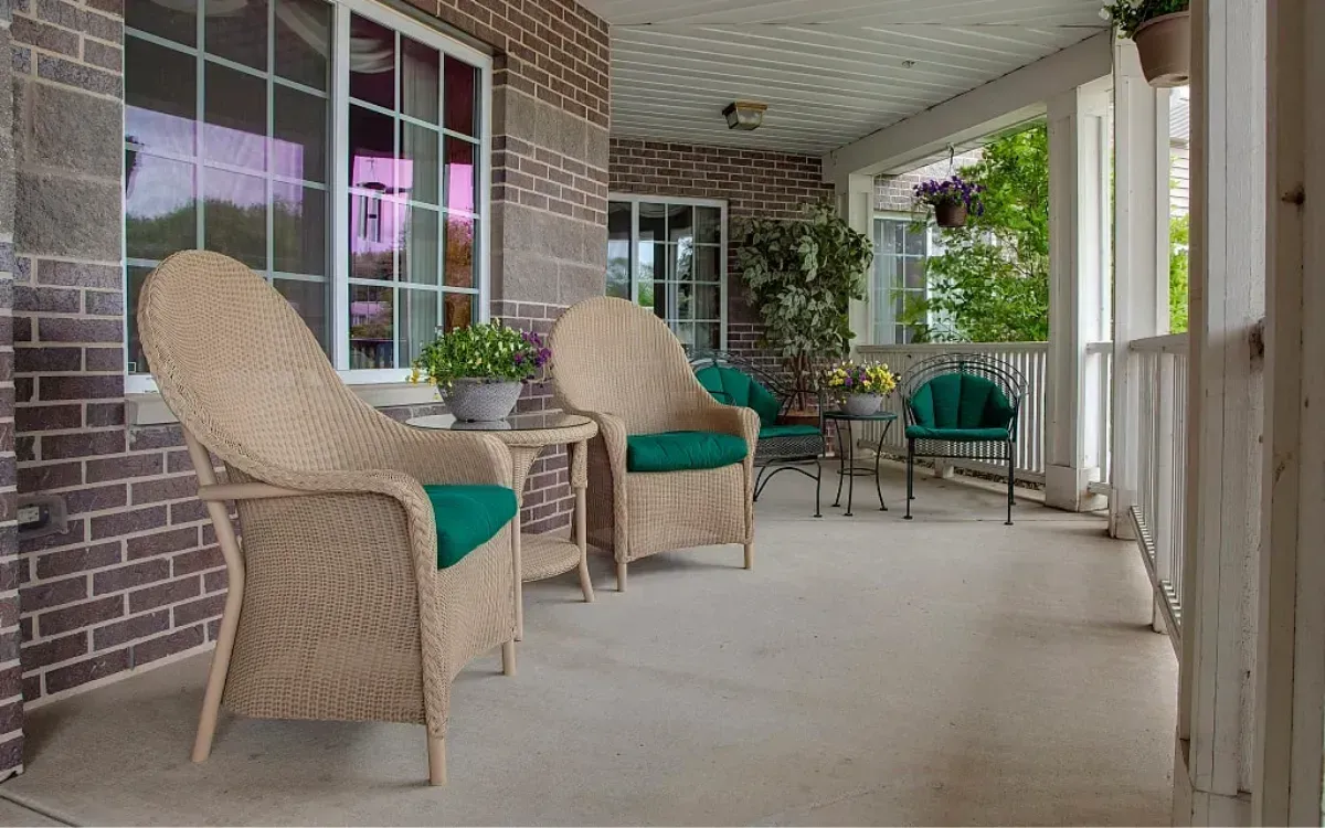 Covered porch with wicker chairs and teal cushions beside brick walls and windows