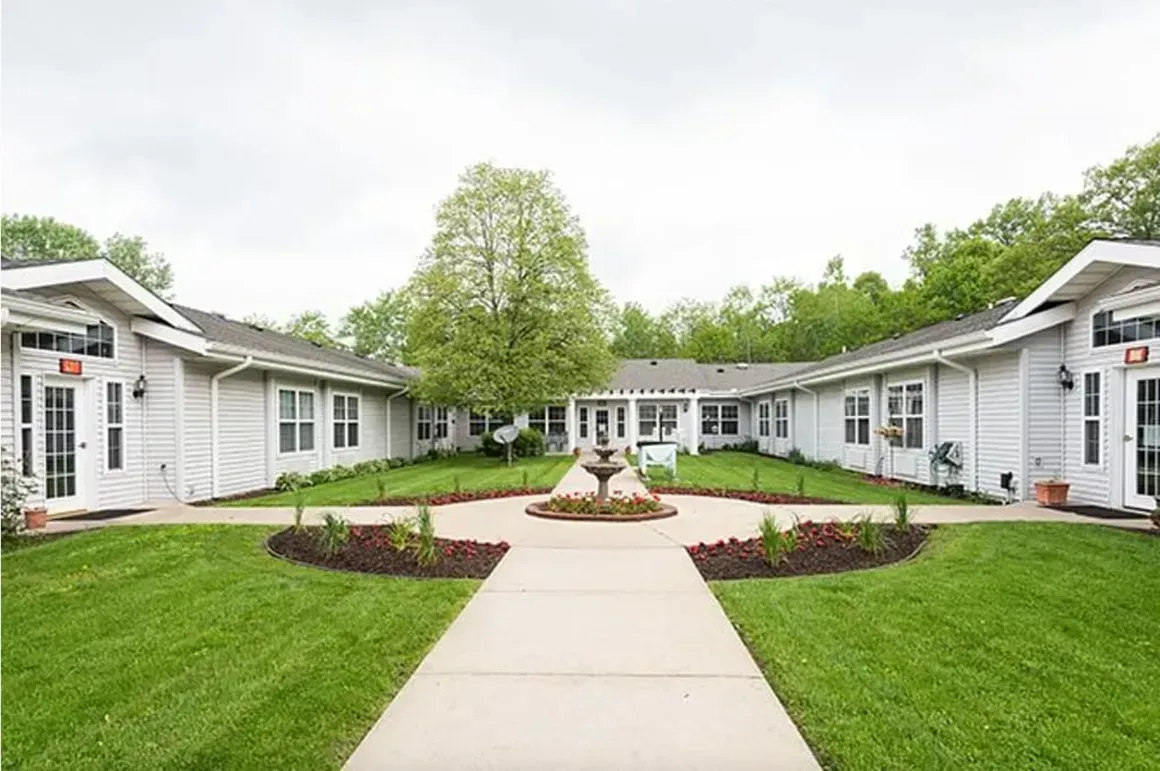 Courtyard of white single-story buildings with a central walkway, fountain, and green lawn