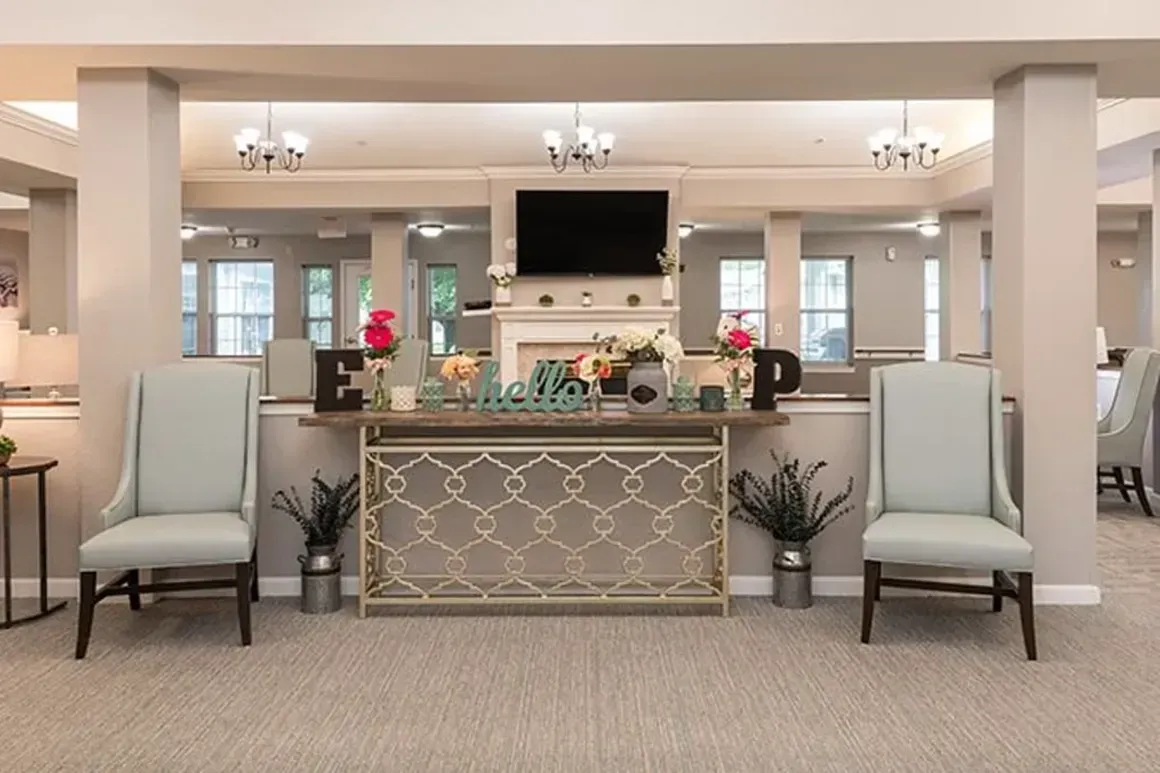 Bright hotel lobby with cream seating, chandelier lights, and a TV above a patterned reception desk