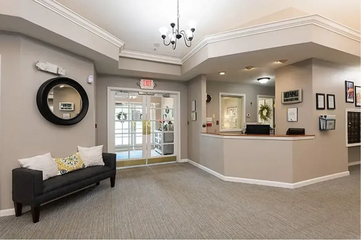 Bright office lobby with glass entrance, reception desk, and black bench with yellow pillows