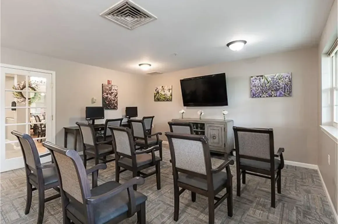 Dining room with six chairs, wall-mounted TV, gray cabinets, and patterned rug in a bright beige interior