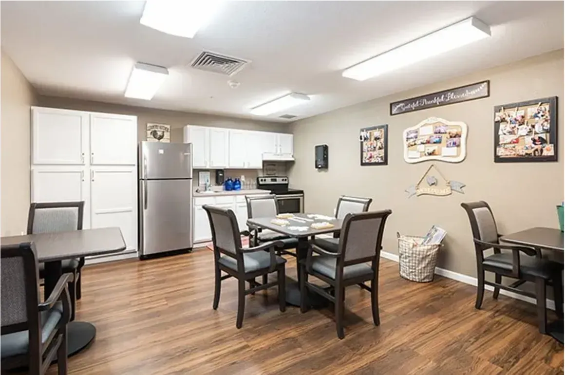 Community room with tables, chairs, kitchenette, and wall art on wood floors