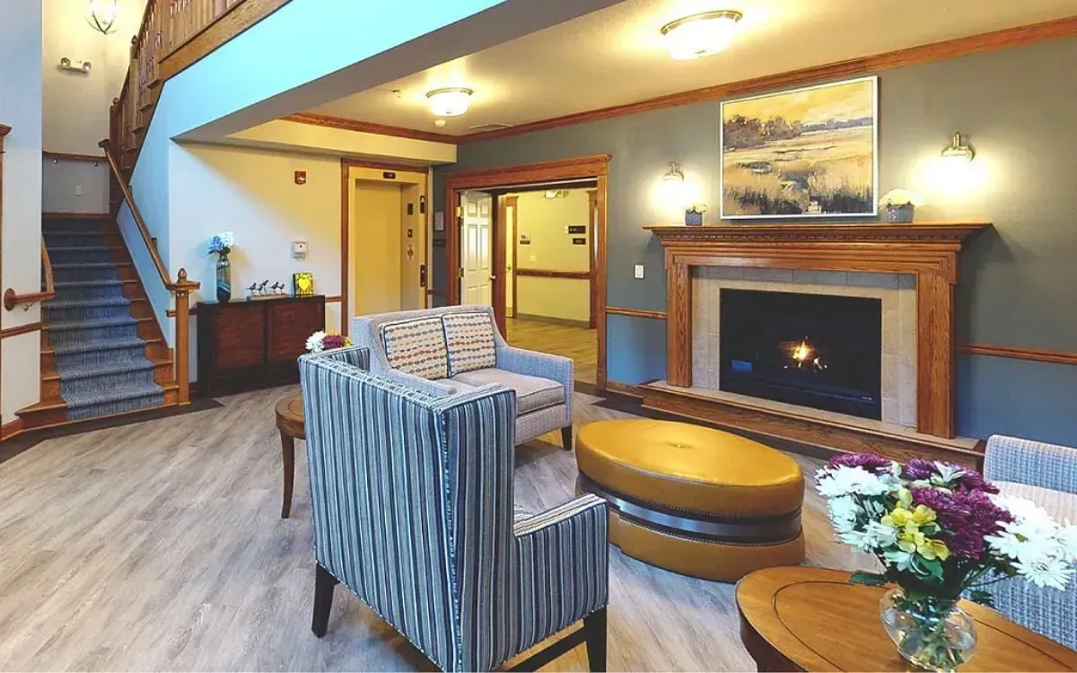 Cozy living room with striped armchairs, fireplace, staircase, and warm lighting