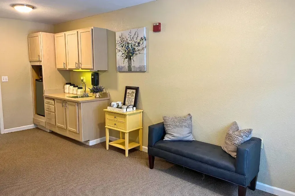 Apartment lounge with kitchenette, small yellow table, and dark blue sofa against a beige wall.