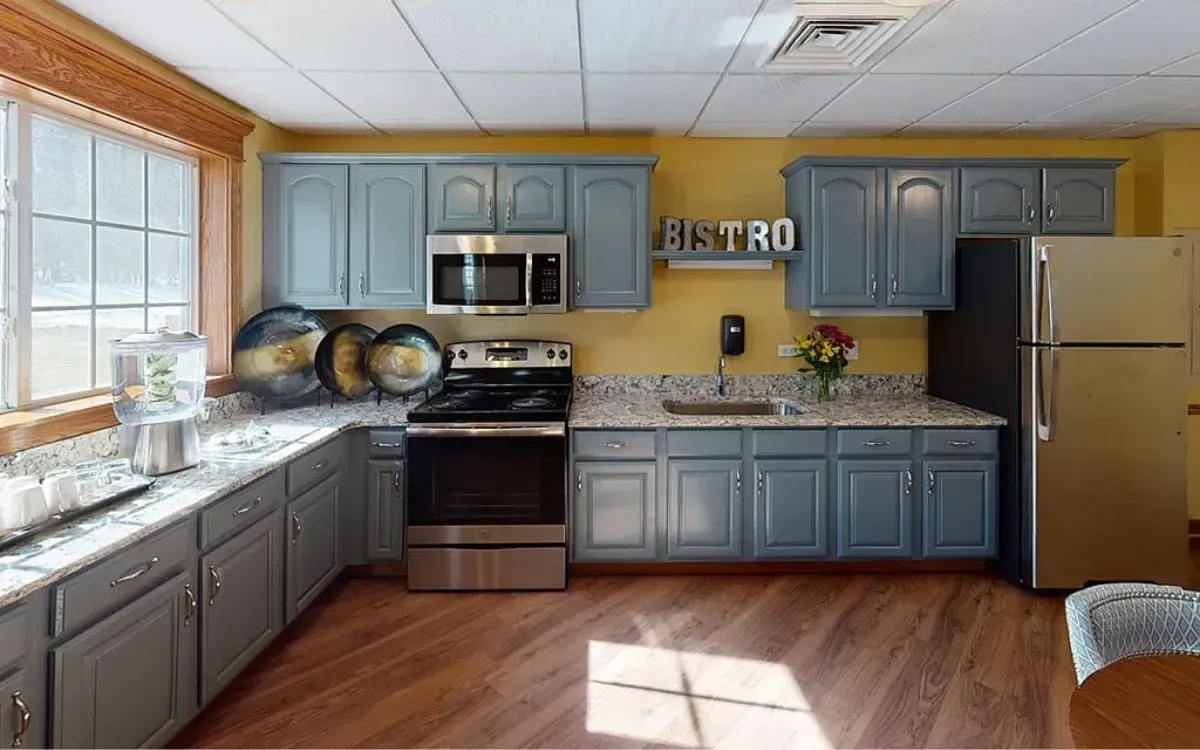 Bright kitchen with gray cabinets, stainless appliances, wood floor, and a large window over the sink