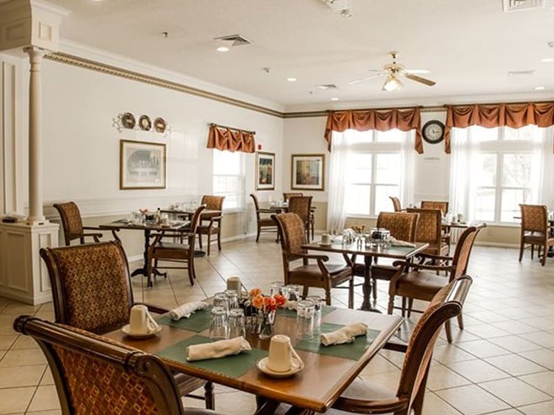 Bright dining room with wicker chairs, set tables, and large windows with curtains