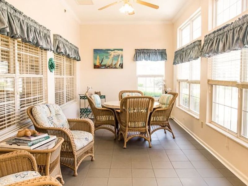 Bright sunroom dining area with wicker table and chairs, tiled floor, and large windows with blinds