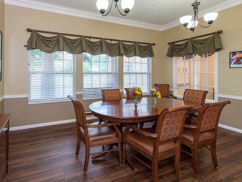 Dining room with a wooden table and chairs, large windows, and green valances above the blinds.