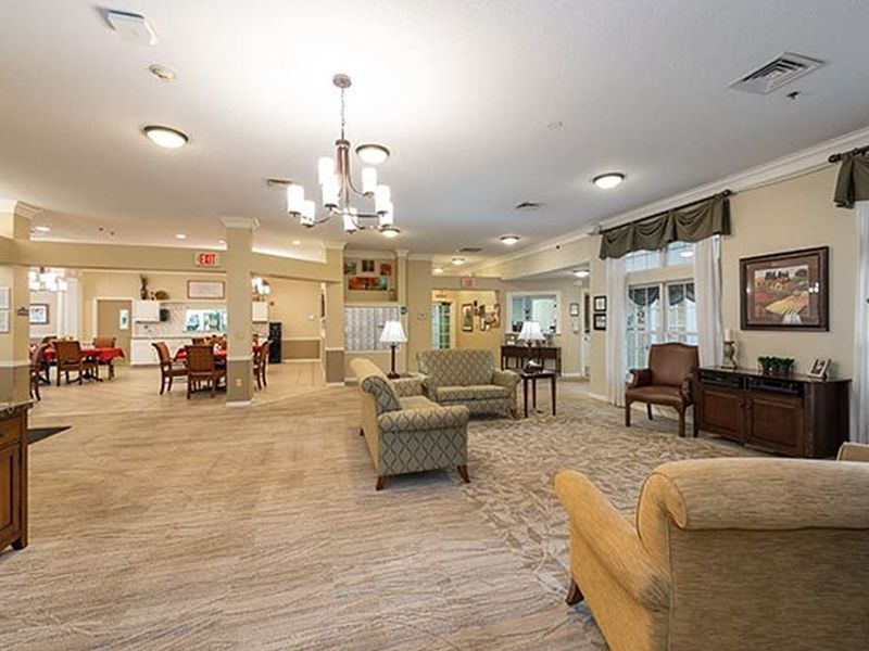 Bright assisted-living lounge with sofas, chairs, tables, and warm overhead lighting