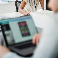 Blurred office scene with a person using a laptop in the foreground and another seated in the background