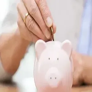 Hand placing a coin into a pink piggy bank on a table