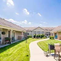Sunny courtyard with curved walkway, green lawn, and patio chairs between beige apartment buildings