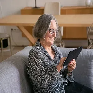 Smiling woman on a gray sofa using a tablet in a bright living room