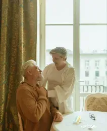 Two people sharing a warm conversation beside a sunlit window and round table