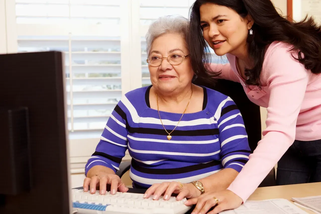 Woman helping an older woman use a computer at a desk indoors