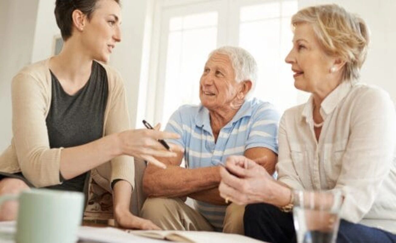 Three people talking in a bright living room, with one woman gesturing while the others listen