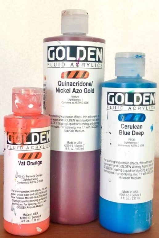 Three bottles of Golden Fluid Acrylic paint in red, orange, and blue colors.
