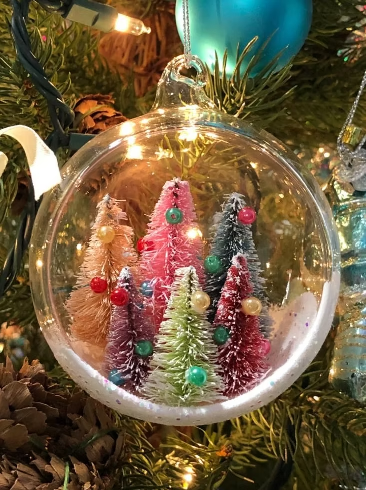 Clear glass Christmas ornament with miniature colorful trees and snow.