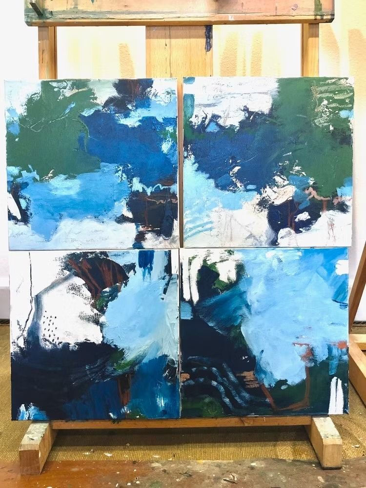 Four square abstract paintings on an easel. Blues, greens, and whites in a layered composition.