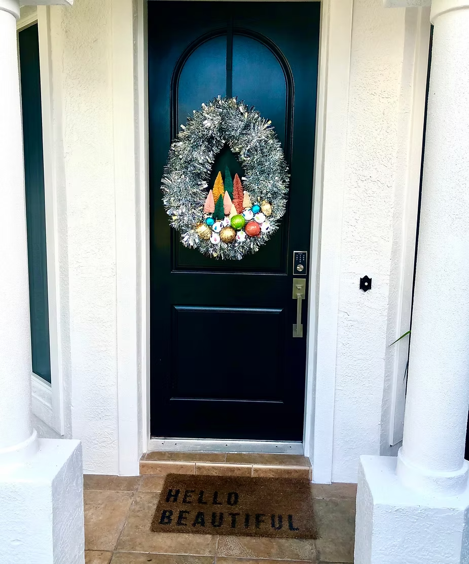Black front door with silver wreath, colorful ornaments, and 