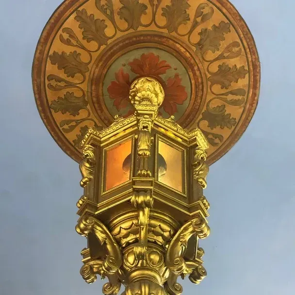 Ornate gold chandelier attached to a painted ceiling medallion with leaf patterns.