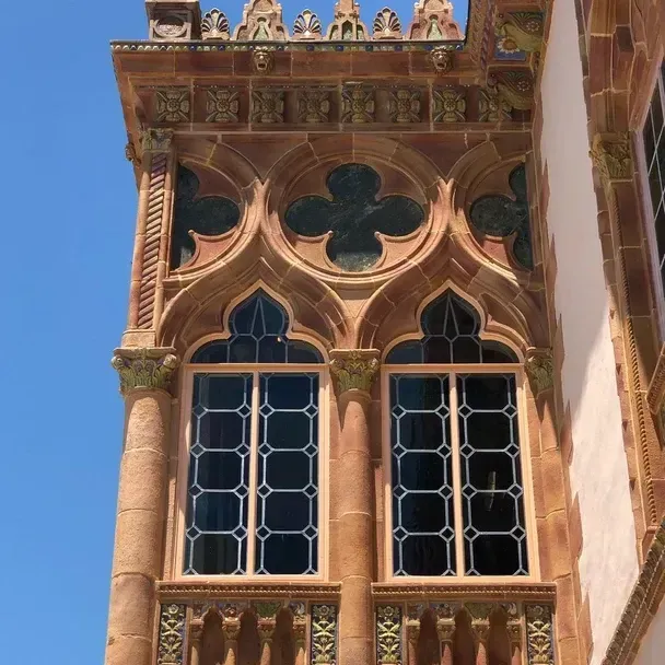 Ornate, terracotta-colored building facade with arched windows, decorative trim, and a clear blue sky.