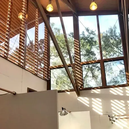 Shower with large windows, wooden beams, and slatted blinds. Sunlight streams in.